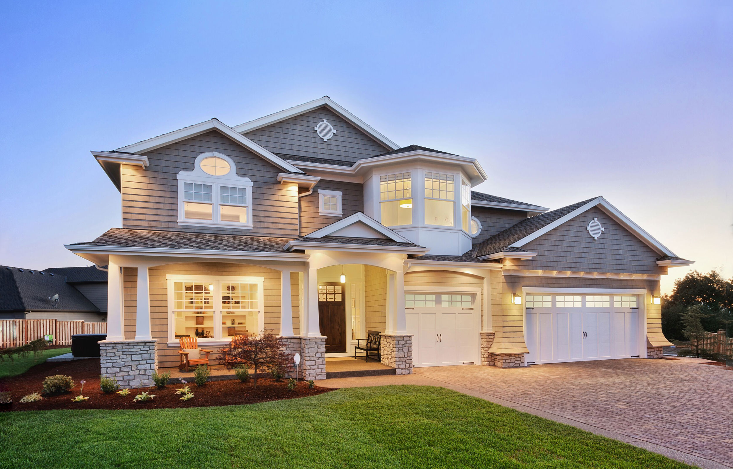 Large two-story house at dusk with exterior lights on and a three-car garage.