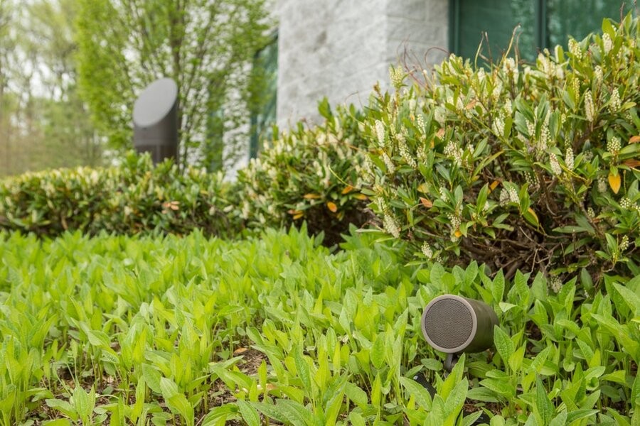 Two differently sized Coastal Source speakers in a backyard surrounded by grass and foliage.