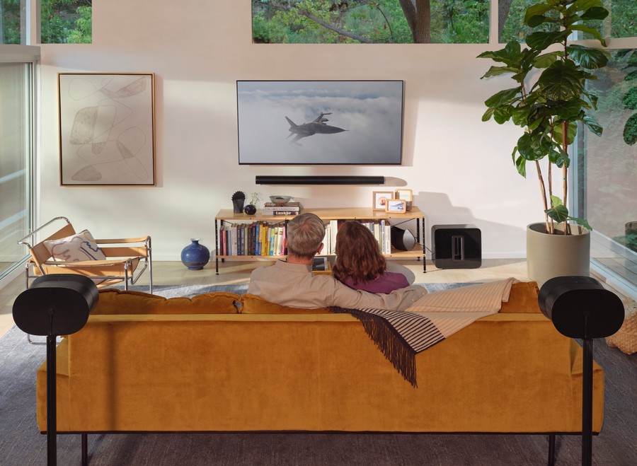 Two people in a room watching a movie with a Sonos surround sound system. 