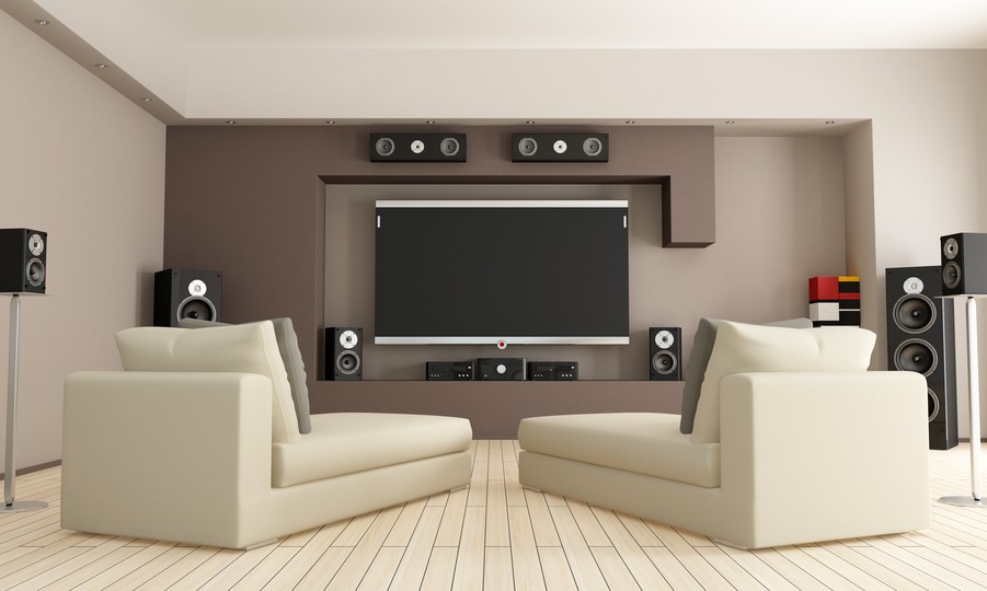 Image is of a beige living room with surround-sound speakers mounted on the wall.