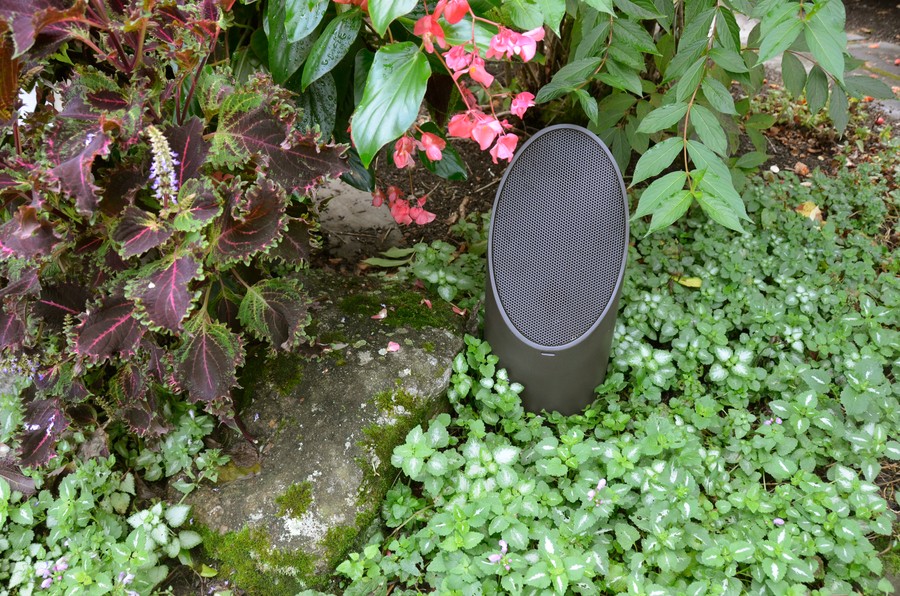 A mini-bollard outdoor speaker nestled neatly within a colorful garden.