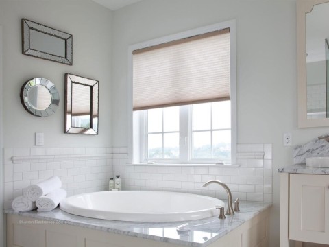 A large bathtub underneath a window with motorized shades.