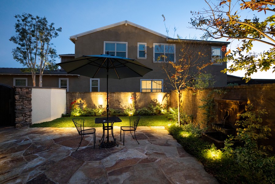 A beautiful backyard with an outdoor patio, lit up at dusk. 