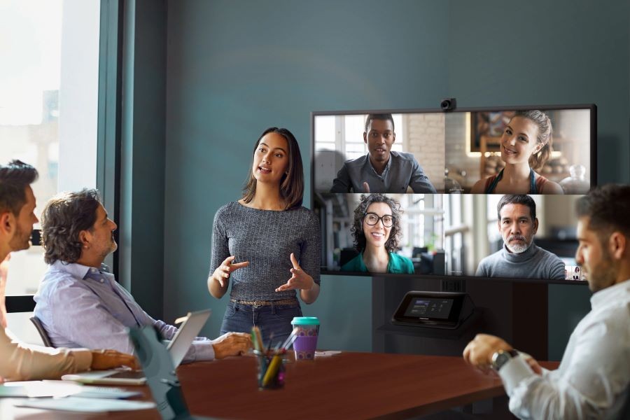 A video conference meeting with one person presenting, three sitting at a table, and four remote participants.